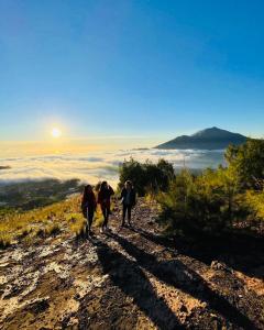 three people walking up a hill with the sun in the background at Batur Caldera Guesthouse in Kintamani