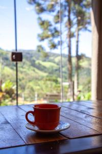 a red coffee cup on a wooden table with a window at Oca Roça in Delfim Moreira