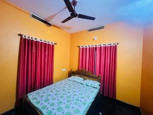 - une chambre avec des rideaux rouges et un lit avec un ventilateur de plafond dans l'établissement Paddy View Service Villa, à Wayanad