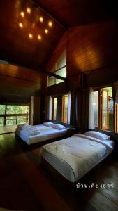 two beds in a large room with windows at บ้านเคียงธาร โฮมสเตย์ แม่แมะ Cascade Lodge in Amphoe Chiang Dao