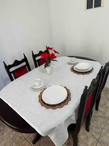 una mesa con platos blancos y un jarrón con flores rojas en Apto 2 quartos próx. Floripa Shopping, en Florianópolis