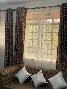 a couch with pillows sitting in front of a window at Dzefry Homes in Nakuru