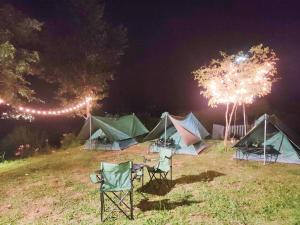 un groupe de tentes et de chaises dans un champ la nuit dans l'établissement บ้านพักเกชิลตา เขาค้อวิวทะเลหมอก, à Khao Kho