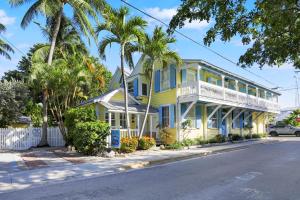 a yellow house with a white porch and palm trees at Tranquillity Guest House in Key West