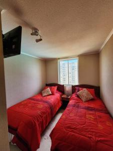 two beds in a room with red sheets and a window at Departamento Laguna Vista in Algarrobo