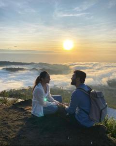 a man and woman sitting on top of a mountain at sunset at Batur Caldera Guesthouse in Kintamani