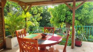 una mesa de madera y sillas en un porche con árboles en Noukatchimbe Bungalow avec piscine partagée pour 2 à 4 personnes en Le Marin