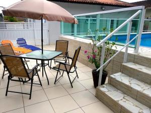 une terrasse avec une table, des chaises et un parasol dans l'établissement CASA JD SÃO LOURENÇO PISCINA AR WI-FI TV PRAIA, à Bertioga