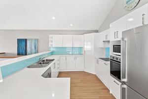 a white kitchen with white cabinets and blue accents at Beach Duplex 72 Marine Dr - Fingal Bay in Fingal Bay