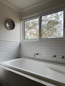a white bath tub in a bathroom with two windows at Summit House Armidale - 2 or 4 Bedrooms in Armidale