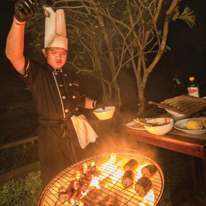 a chef standing next to a grill with food at Ayawana Private Villas Managed by ARM Hospitality in Tegalalang