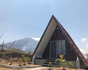 a house with a pointed roof with mountains in the background at Villa Eger Rinjani in Sembalun Lawang