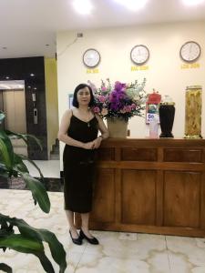 kobieta w czarnej sukience stojąca przed ladą w obiekcie Quỳnh Hương Hotel Phú Thọ w mieście Phú Thọ