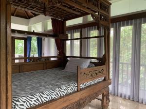 a wooden canopy bed in a room with windows at Large House with Swimming Pool-Griya Alcheringa in Bedoyo