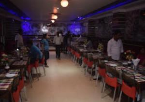 a room filled with tables and chairs with people standing around at Hotel Midway & Zaika Restaurant Bihar in Madhipura