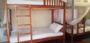 two bunk beds with white sheets and a ladder at Jinja Backpackers in Jinja