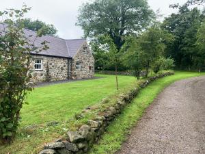 a stone house with a stone wall next to a road at RB Contractor Stays - Helyg in Pwllheli