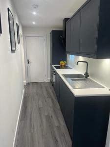 a kitchen with black cabinets and a sink and wood floors at The Boyd - Coorie Doon in Prestwick