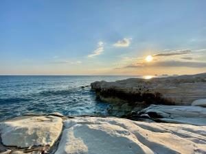 a sunset over the ocean with rocks in the water at Cyprus Villages Hotel & Restaurant - Central Location - Bed & Breakfast - With Access To Pool And Stunning Views in Tochni