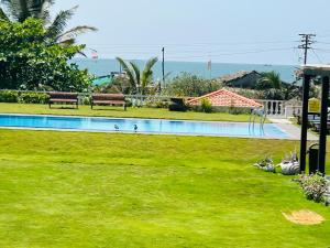 uma piscina com relva verde e bancos num quintal em Resort Terra Paraiso em Calangute