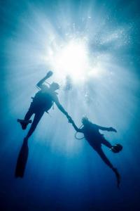 two people in the water with the sun behind them at Ocean Voice Beach Resort & Diving in Nolhivaranfaru