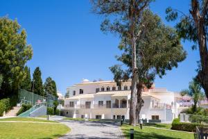 a large white building with a tree in the foreground at Clube Vilarosa in Portimão