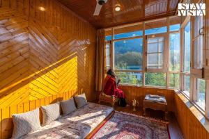 una mujer sentada en una habitación mirando por la ventana en StayVista at Qaraar - Preng en Srinagar