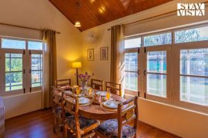uma sala de jantar com mesa, cadeiras e janelas em StayVista at Qaraar - Preng em Srinagar