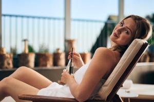 a woman sitting in a chair holding a cell phone at Pohorje Village Wellbeing Resort - Wellness & Spa Hotel Bolfenk in Hočko Pohorje +135 photos