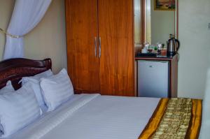 a bedroom with a bed with white sheets and a wooden cabinet at La Grande Hotel in Kampala +55 photos