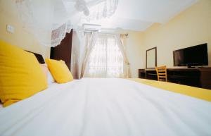 a bedroom with a large bed with yellow pillows and a television at City Hill Hotel in Bujumbura