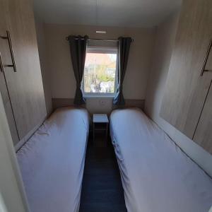 two beds in a small room with a window at Chalet Weizicht op minicamping Hoogelande in Grijpskerke