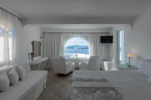 a white bedroom with a bed and a desk and a window at Caldera View Private Villa in Megalochori