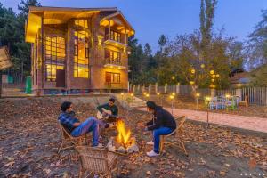 four men sitting around a fire in front of a house at Zostel Pahalgam in Pahalgām