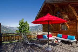 une terrasse en bois avec un parasol et des chaises rouges dans l'établissement Chalet Kala, à Risoul