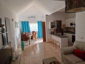 ein Wohnzimmer mit einem Sofa und eine Küche mit blauen Vorhängen in der Unterkunft Villa Juanita, Puerto del Carmen, Lanzarote in Tías
