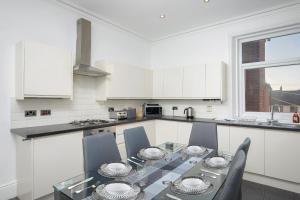Lytham Place في بلاكبول: مطبخ أبيض مع طاولة وكراسي زجاجية