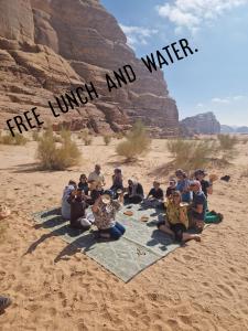 Un gruppo di persone sedute su una coperta nel deserto di Sky Light Wadi Rum a Wadi Rum