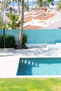 a blue swimming pool next to a building with a palm tree at Vivienda Vacacional Pasito Blanco 1 in Pasito Blanco