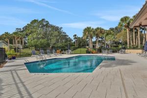 a swimming pool with chairs and tables and trees at Ocean’s Treasures Retreat Beach Condo in Ponte Vedra Beach