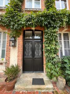 uma porta preta da frente de uma casa de tijolos com hera em Maison d'hôtes l'Évidence em Rugles