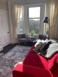 a red couch in a living room with a window at Beautiful traditional flat in the center of Largs. in Largs