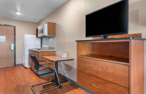 Extended Stay America Select Suites - Jacksonville - North في جاكسونفيل: غرفة بها مكتب وتلفزيون على خزانة