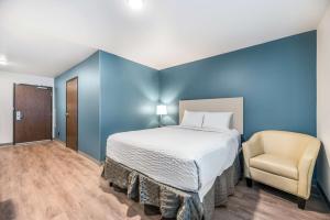 Extended Stay America Select Suites - Orlando - Kissimmee في أورلاندو: غرفة نوم زرقاء مع سرير وكرسي
