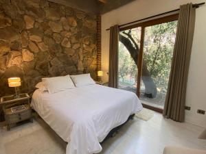 1 dormitorio con cama y pared de piedra en Iluminada casa de piedra entre bosque y río, en Lo Barnechea