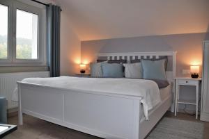 a white bedroom with a large white bed with blue pillows at Superior - Ferienhaus am Engelsbach im Thüringer Wald in Engelsbach