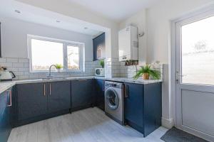 een keuken met blauwe kasten en een wasmachine en droger bij New Stylish 5BD, 5min from town in Cardiff