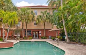 a swimming pool in front of a building with palm trees at Extended Stay America Premier Suites - Fort Lauderdale - Cypress Creek - Park North in Pompano Beach