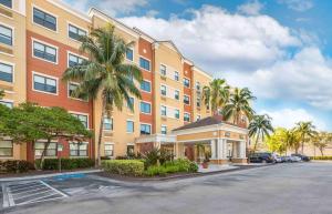 a building with a palm tree in front of a parking lot at Extended Stay America Premier Suites - Miami - Airport - Doral - 25th Street in Miami