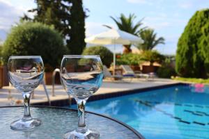 two wine glasses sitting on a table near a swimming pool at Olive Villa Crete in Rethymno Town